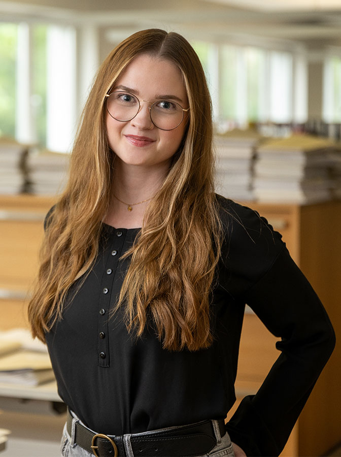 Portraitfoto einer jungen Frau mit Brille und dunklem, legeren Oberteil