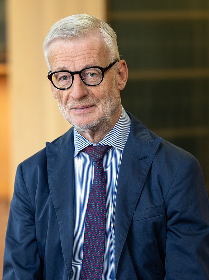 Portraitfoto eines älteren Herren mit Brille und blauem Anzug