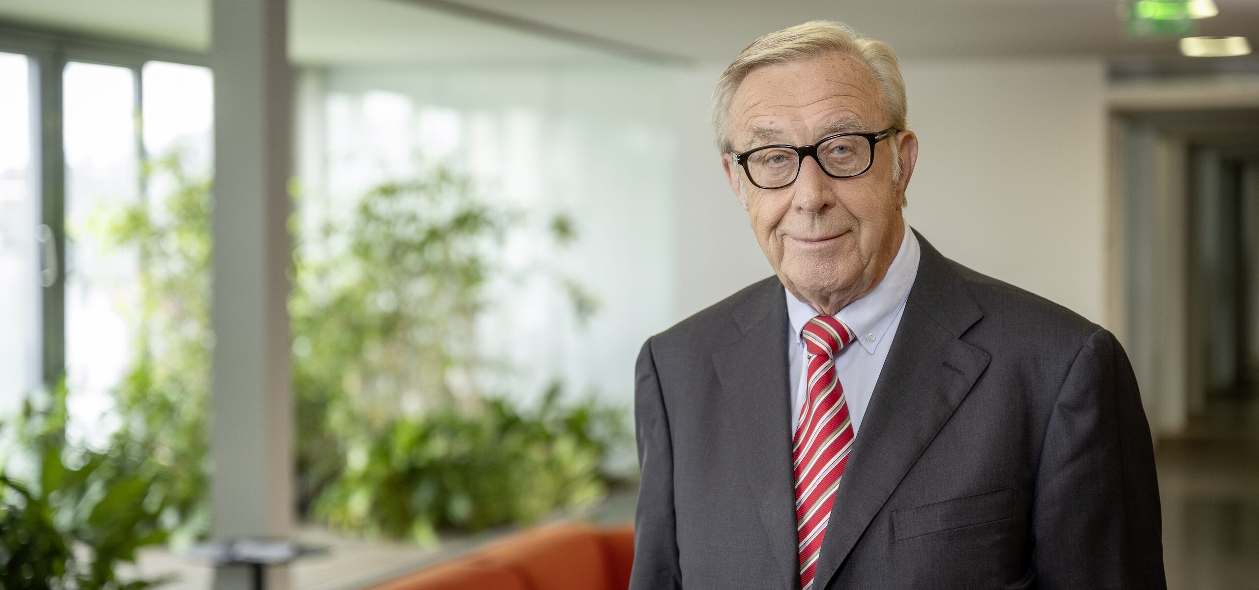 Portraitfoto eines älteren Herren mit dunkelgrauem Anzug und roter Krawatte